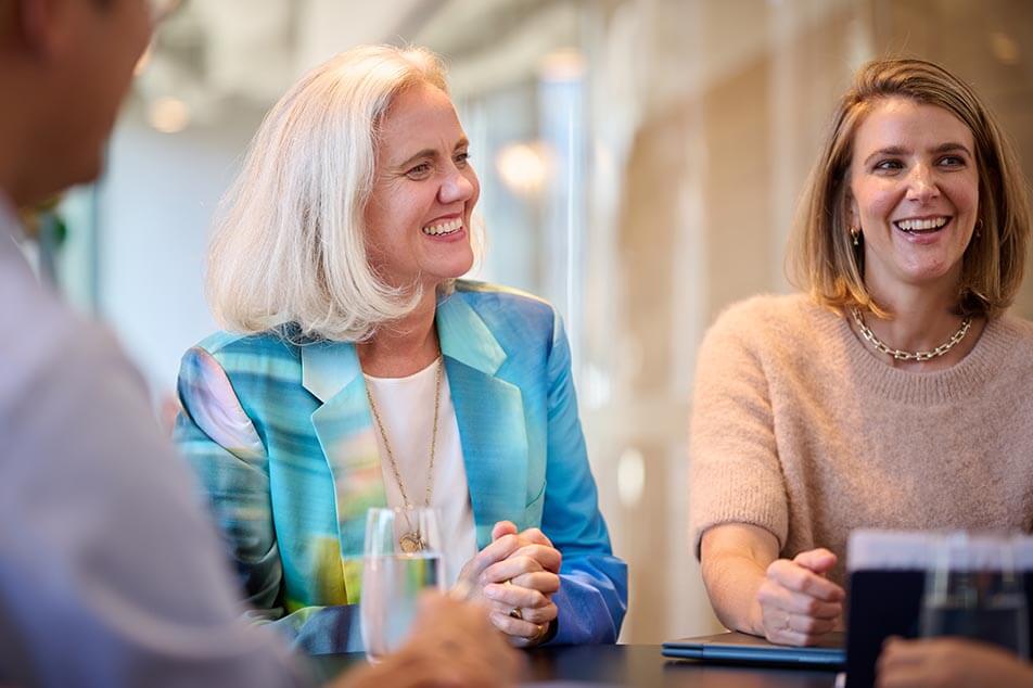 Two office workers sitting side by side smiling at people opposite them