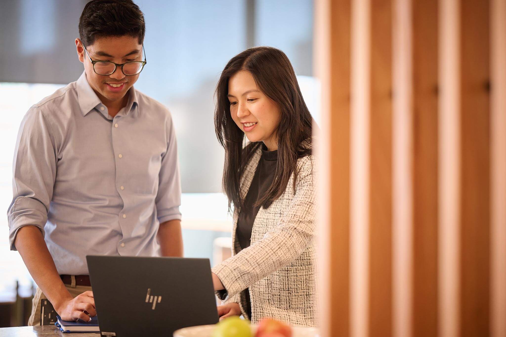 Two office workers standing looking at something on a laptop