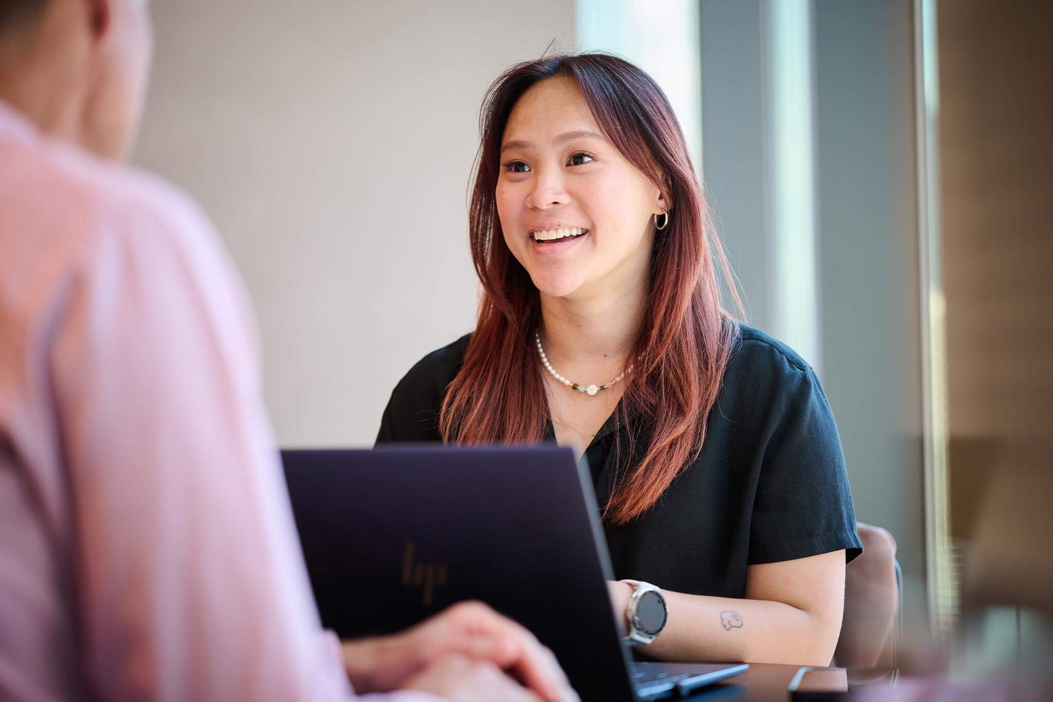 An office worker in front of a laptop interacting with another worker facing her